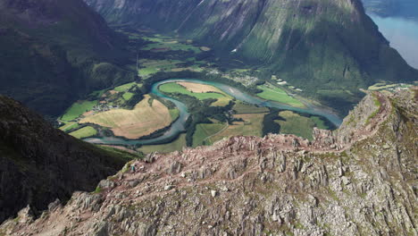Two-Hikers-Walking-on-the-Edge-of-a-Stunning-Breathtaking-Ridge-in-Norway,-Romdalseggen,-Aerial-View-of-a-Mountain-Landscape-with-a-Beautiful-River-in-the-Background