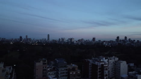 Drone-rises-up-over-a-park-in-Buenos-Aires,-evening-city-view