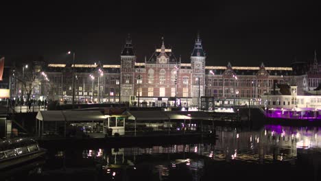 Estación-Central-De-Amsterdam,-Países-Bajos,-Depósito-De-Trenes-Por-La-Noche-Por-El-Canal-Iluminado-En-El-Centro-De-Invierno