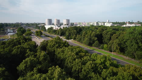 Aerial-forward-flight-over-forest,-road-and-residential-block-district-of-Warsaw-in-background