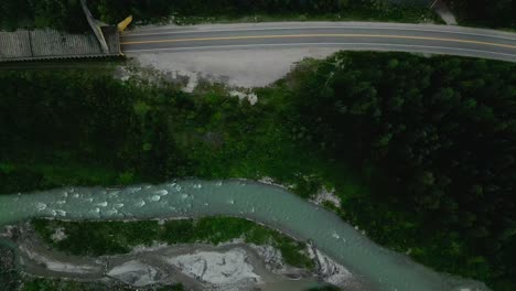 Drone-flying-over-a-mountain-river-beside-a-sheltered-highway
