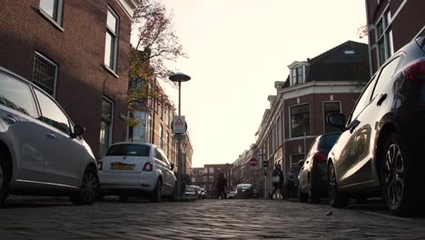 Amsterdam-Netherlands-city-cobblestone-street-with-cars-and-apartment-buildings-in-background-at-sunset