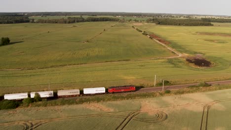 Following-a-DB-Schenker-cargo-train-driving-through-Germany-countryside,-aerial