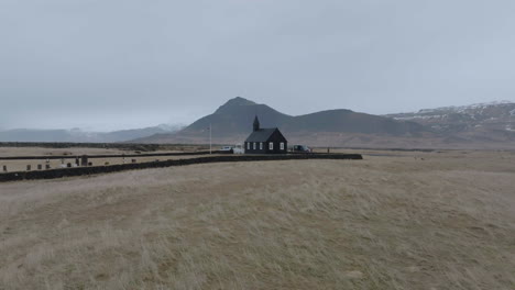 Drone-Shot-of-Church-in-Búðir,-Iceland,-Black-Building-in-Humid-Landscape-on-Cloudy-Day