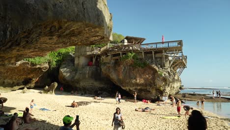Suluban-Strand-Auf-Bali,-Indonesien-Mit-Sand-Und-Menschen-Zwischen-Zwei-Klippen-An-Einem-Sonnigen-Tag-Voller-Surfer-Und-Schwimmer-Und-Einer-Bar-Auf-Einem-Felsen