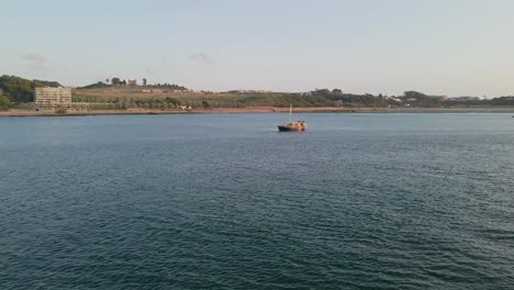 Fly-Over-Douro-River-Estuary,-Little-boat-sailing-at-sunset