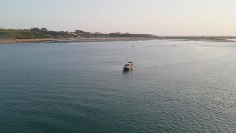 Boat-at-sunset-in-Douro-River-estuary,-Porto,-Portugal---Aerial-tracking