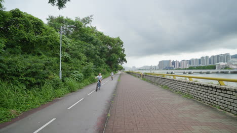 Ciclismo-Urbano:-Toma-De-Cardán-De-Carril-Bici-Con-Río-Y-Paisaje-Urbano-En-Hong-Kong