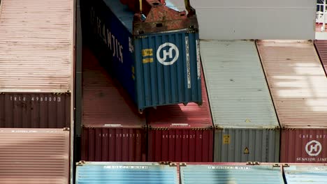 Harbor-crane-loads-blue-container-to-a-cargo-ship-for-export,-static-telephoto