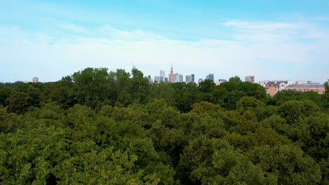 Descending-drone-shot-showing-skyline-of-Warsaw-City-and-dense-green-forest-in-foreground---Capital-of-Poland-during-sunny-day