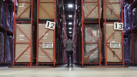 A-BIPOC-Ashley-Furniture-HomeStore-warehouse-merchandise-worker-walks-between-two-distribution-center-racks-to-check-the-inventory-using-a-clip-board