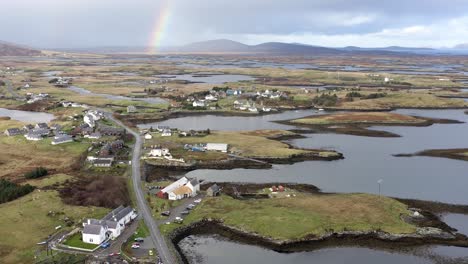 Wide-angle-drone-shot-of-the-landscape-around-Lochmaddy-on-the-island-of-North-Uist,-featuring-the-moor-and-peatland,-a-rainbow,-the-distant-mountains,-lochs-and-residential-buildings