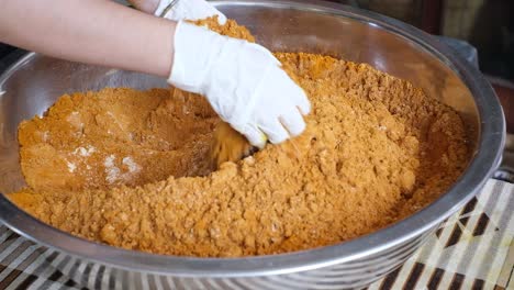 Close-up-scene-of-a-woman-mixing-ginger-and-turmeric-powder,-both-hands-wearing-safety-gloves-mixing-the-powder