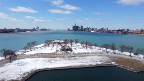 Snow-covered-Belle-isle-and-vast-Detroit-river-with-skyline,-aerial-view