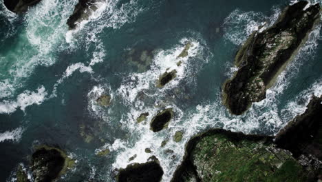 Aerial-top-down-angle-side-dolly-drone-footage-of-ocean-blue-waves-break-on-high-cliff-of-a-rocky-mountain