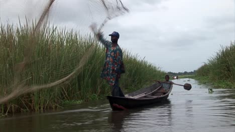 Fischer-Wirft-Das-Netz-Mit-Einem-Kleinen-Jungen-Auf-Einem-Boot-In-Nigeria