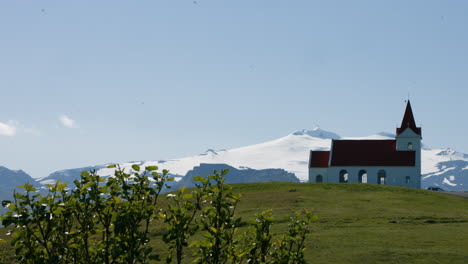 Stone-church-Ingjaldsholskirkja-on-green-hill,-Snæfellsjökull-glacier-behind