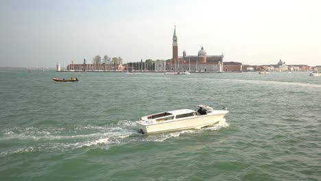 Ein-Weißes-Vaporetto-Boot-Segelt-Von-Links-Nach-Rechts-Auf-Dem-Meer,-Im-Hintergrund-Die-Stadt-Venedig