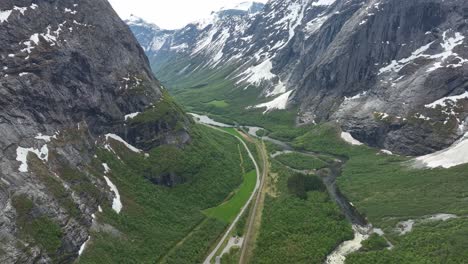 Stunning-Romsdalen-valley-close-to-Trollveggen-mountain-wall-in-Norway---High-altitude-aerial-above-lush-green-valley-with-road,-railway-and-river---Snow-in-mountains