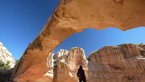 Lonely-Woman-Standing-on-Rock-Under-Natural-Sandstone-Arch,-Hickman-Bridge,-Capitol-Reef-National-Park,-Utah-USA