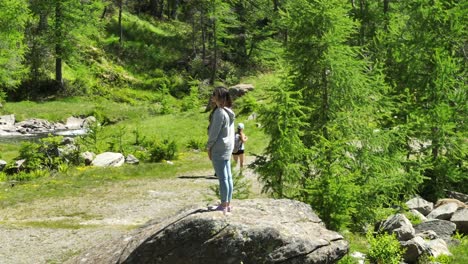 Woman-standing-on-rock-and-hikers-or-trekkers-walking-surrounded-by-nature-of-Val-Masino-in-Valtellina,-Italy