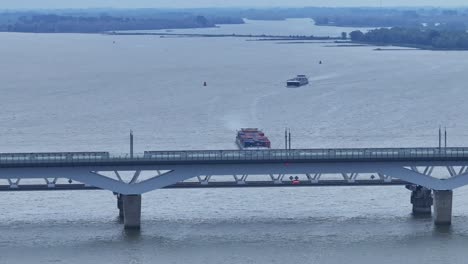 Descending-drone-view-of-the-cargo-ship-Alfa-Menta-makeing-its-way-towards-the-Moerdijk-bridges,-its-powerful-engines-propelling-it-through-the-water-as-it-approaches-the-low-bridge