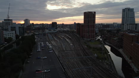 Establishing-Drone-Shot-Approaching-Leeds-City-Centre-and-Train-Station-at-Sunrise-with-Train-Leaving-Station-in-Low-Light