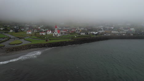 Sandavagur-village,-Vagar-island:-circling-aerial-view-to-the-village-church-on-a-foggy-day