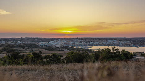 High-angle-shot-over-the-seaside-town-in-Marsaxlokk,-Malta-with-sun-rising-in-the-background-in-timelapse