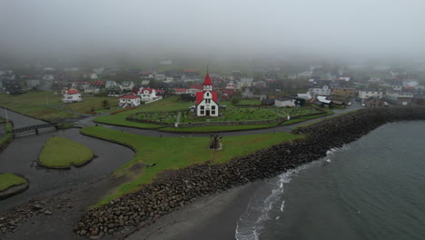 Sandavagur-village,-Vagar-island:-aerial-view-traveling-out-to-the-church-and-the-village-from-the-coast