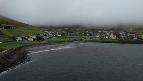 Sandavagur-village,-Vagar-island:-aerial-view-in-orbit-from-the-coast-to-the-village-and-the-church-in-the-Faroe-Islands