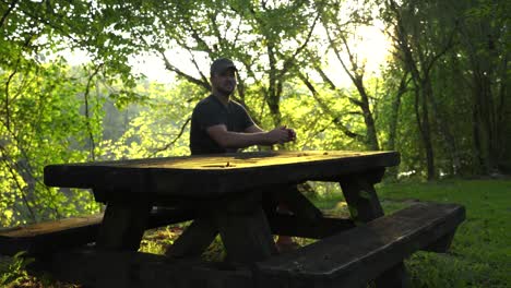 Man-walks-up-and-sits-at-a-picnic-table