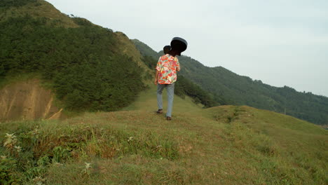 Guitar-Music-Player-Walk-Through-Green-Hills-Landscape,-Vintage-Colorful-Clothes-Hawaiian-Shirt,-Jeans-and-Boots