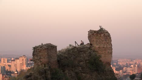 Hombre-Aventurero-Trepando-A-La-Ruina-Con-Vistas-A-Tbilisi-Al-Atardecer