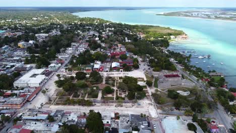 Aerial-view-of-Bacalar-Mexico-Quintana-Roo-drone-fly-above-Mexican-tourist-village-dotted-with-resort-on-tropical-sandy-beach-and-blue-lake-lagoon