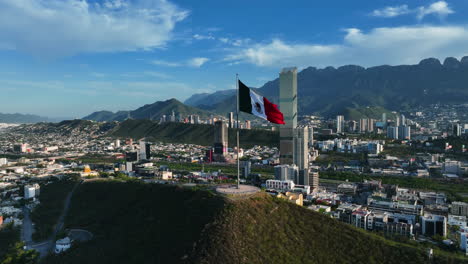 Aerial-view-around-a-mexican-flag-on-top-of-the-Cerro-del-Obispado,-golden-hour-in-Monterrey,-Mexico