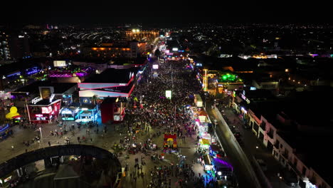 Drone-shot-backwards-over-crowds-at-the-San-Marcos-fair,-nighttime-in-Aguascalientes,-Mexico
