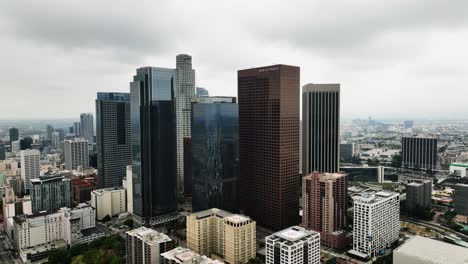 Aerial-view-away-from-skyscrapers-in-downtown-Los-Angeles,-in-cloudy-USA---pull-back,-drone-shot