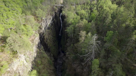 Aerial-drone-shot-flying-away-from-waterfall-inside-narrow-Corrieshalloch-gorge-surrounded-by-forest-in-Scottish-Highlands