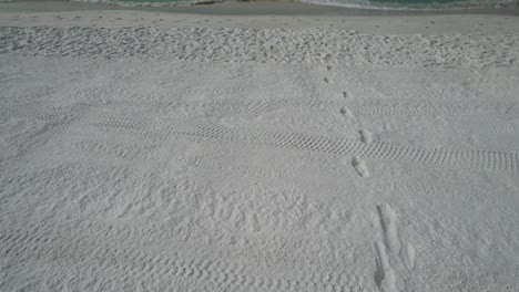 Aerial-view-of-foot-prints-on-the-white-sands-of-Florida-to-the-clear-emerald-waters-of-the-Gulf-of-Mexico-on-a-bright-sunny-summer-day