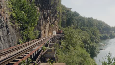 A-distant-train-about-to-cross-the-Tham-Krasae-Railway-Bridge,-part-of-the-death-railway-which-runs-along-the-Kwai-River,-Kanchanaburi-Thailand