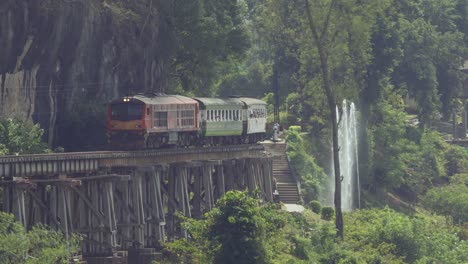 A-train-crossing-over-the-old-wooden-Tham-Krasae-Railway-Bridge,-a-popular-tourist-attraction-in-Kanchanaburi-Thailand