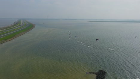 6-kitesurfers-in-a-line-riding-towards-the-Afsluitdijk-in-The-Netherlands,-drone-shot