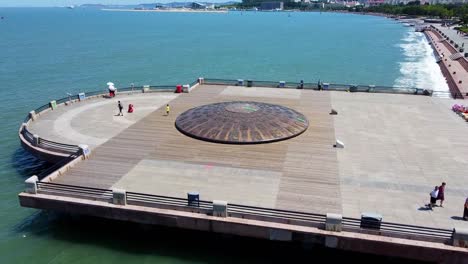 Cinematic-aerial-forward-dolly-plus-tilt-down-view-of-famous-touristic-pier-wharf-with-mini-dome-full-of-ancient-asian-chinese-japanese-religious-inscriptions-characters-in-Weihai,-China