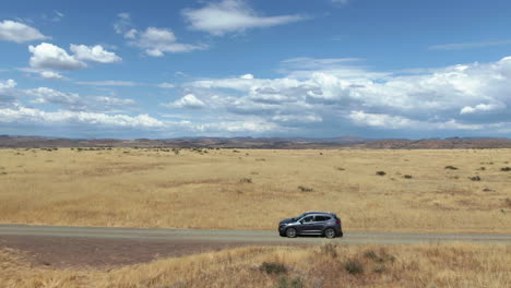 Drone-shot-tracking-a-EV-car-driving-in-middle-of-remote-prairie-on-a-sunny-day
