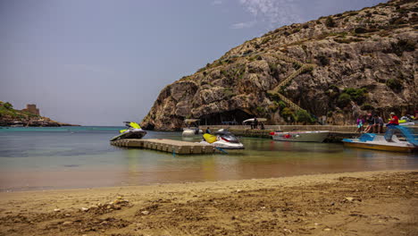 Lapso-De-Tiempo-De-Varios-Barcos,-Navegantes-Y-Esquiadores-Acuáticos-En-Un-Muelle-En-La-Playa-De-Xlendi-En-Malta