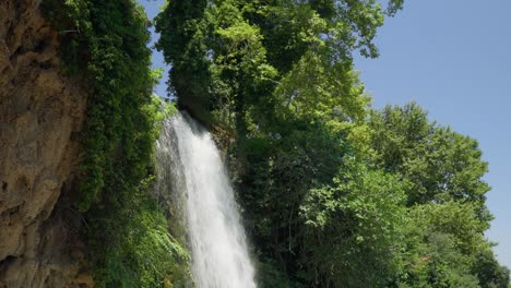 Zeitlupen-Wasserfallaufnahme,-Die-Den-Wald-An-Sonnigen-Sommertagen-Und-Blauem-Himmel-Hinunterschwenkt
