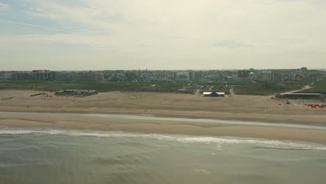 Drone-shot-of-the-popular-beach-of-Noordwijk-in-the-morning,-showing-beach-clubs-and-the-town-in-the-background