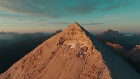 Drone-point-of-view-flying-towards-the-summit-of-Tofana-di-Rozes-in-the-Italian-Dolomites-at-sunrise,-tilting-upwards-to-reveal-the-iconic-summit-cross