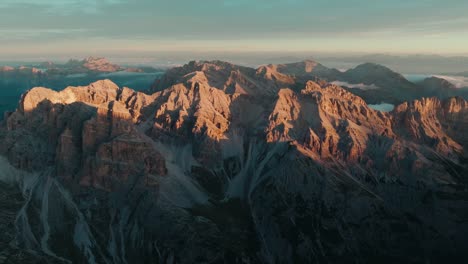 Aerial-view-from-left-to-right-of-the-iconic-Punta-Sud-di-Fanes,-Punta-Nord-and-Monte-Ciaval-peaks-in-the-Dolomites-of-Cortina-D'Ampezzo,-Italy-with-the-first-light-of-sunrise